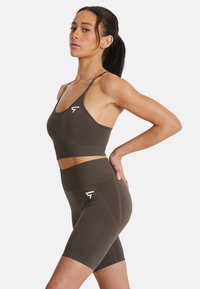 Bra sportivo marrone e pantaloni corti a vita alta abbinati con un design aderente. Presenta accenti del logo bianco su entrambi i capi, realizzati in tessuto morbido.
