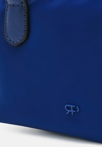 Coin de sac bleu avec détail de sangle texturée et petit logo embossé sur surface lisse sur fond blanc.