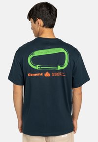 Navy blue cotton T-shirt featuring a large green carabiner graphic on the back with the text "SKATE CO. WORLDWIDE" and orange brand name.