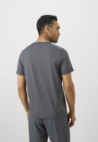 Mann vender bort med en mørkegrå kortermet treningsskjorte med perforert tekst "BORG" på ryggen og matchende shorts.