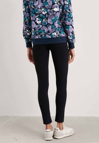 Navy színű, virágmintás pulóver lila és türkiz virágokkal, fekete leggings-szel és logóval díszített fehér sportcipőkkel párosítva.