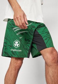Zöld nadrág fekete részletekkel, amely texturált mintával és fehér grafikus csíkokkal rendelkezik. Az alján bal oldalon a "crypto.com" logója található.