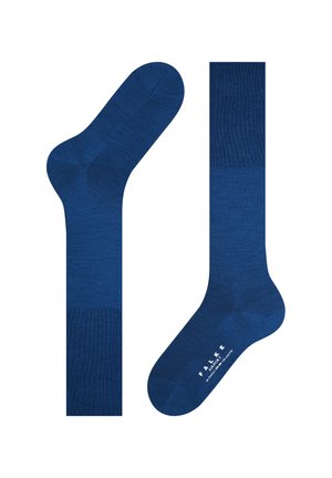 Para długich, solidnych niebieskich skarpet do garnituru z ciemniejszymi niebieskimi mankietami, piętą i palcami, z małym białym nadrukiem tekstu marki na podeszwie stopy.