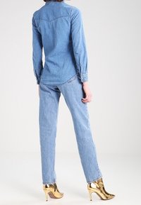 Jeansskjorta och ljusblå jeans kombinerade med metallicguldiga högklackade skor. Skjortan har en klassisk krage och långa ärmar.