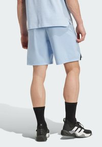 Shorts de sport bleu clair avec une texture lisse, des fentes latérales et une coupe décontractée. Associés à des chaussettes noires et des chaussures de sport noires.
