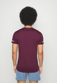 Bordeaux kortärmad skjorta med rund halsringning, tillverkad av mjukt material, med en logotyp på höger ärm och en mjuk, vanlig passform.