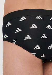 Crne bokserice s geometrijskim bijelim uzorkom trokutastih oblika. Izrađene su od glatke tkanine s crnim elastičnim pojasom.