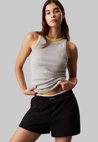 Canotta grigia con accenti gialli, abbinata a pantaloni shorts neri con elastico Calvin Klein. Vestibilità slim e trama del tessuto morbida.