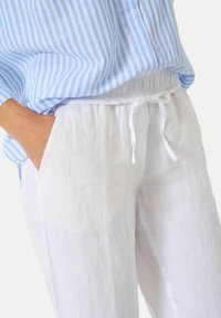 Blouse rayée bleu clair et blanc à coupe décontractée et manches longues, assortie à un pantalon en lin blanc à cordon de serrage avec poches latérales.