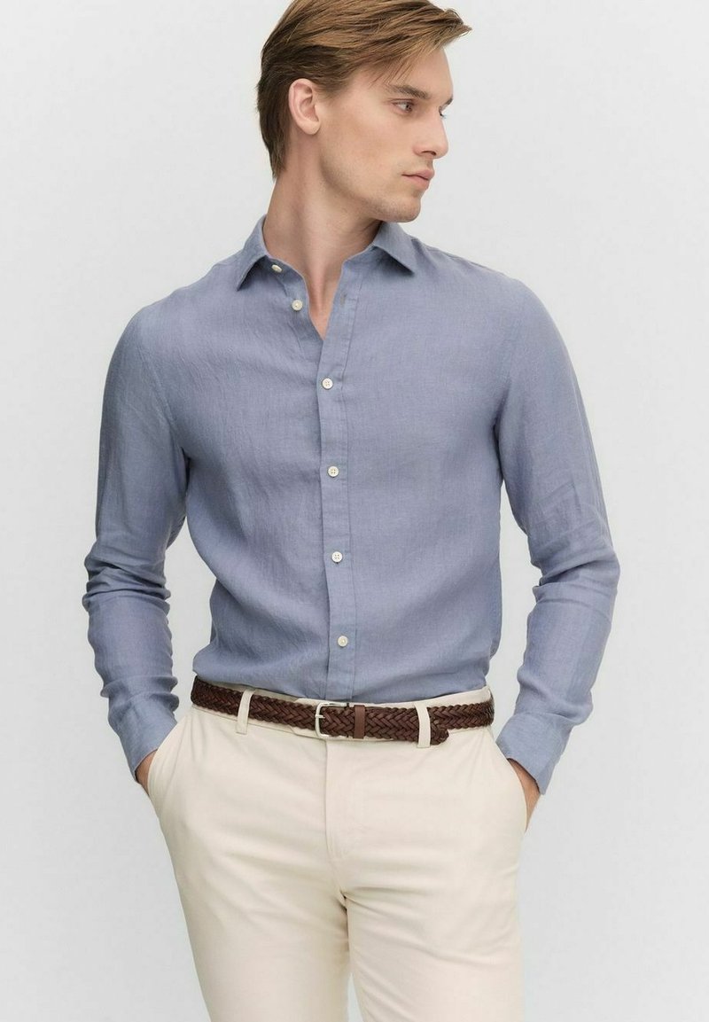 Jasnoniebieska koszula zapinana na guziki z długim rękawem, wykonana z lnu, z kołnierzykiem rozłożonym i luźnym krojem, zestawiona z kremowymi spodniami i brązowym plecionym paskiem.