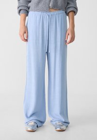 Pantalons larges bleu clair avec une taille à cordon de serrage, fabriqués en matériau doux, présentant une surface texturée et une coupe décontractée.