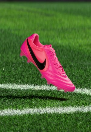 Încălecătură de fotbal Nike roz aprins cu swoosh negru plutind deasupra ierbii verzi, aproape de linia albă a terenului.