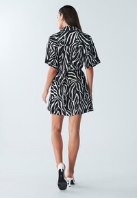 Schwarz-weißes Zebramuster-Kleid mit kurzen Ärmeln, einem Kragen mit Knopfleiste, tailliertem Bund und ausgestelltem Rock, kombiniert mit hochhackigen Mules.