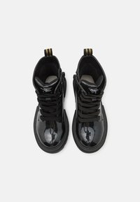 Bottines en cuir verni noir avec une finition brillante, bout rond, lacets noirs, languette de talon rayée jaune et détail de fermeture éclair sur le côté.