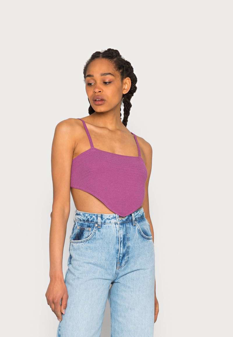 Top crop de malha roxa com alças finas e um hem assimétrico, combinado com jeans de denim azul claro de cintura alta com acentos esmaecidos.