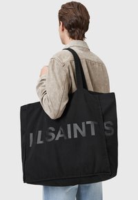 Zwarte canvas schoudertas met groot reliëf "ILSAINTS" logo. Voorzien van stevige schouderbanden en een ruime rechthoekige vorm.