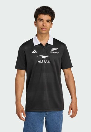 Polo shirt de sport noir avec col blanc, arborant le logo "ALL BLACKS", la marque "ALTRAD" et un tissu texturé. Coupe décontractée, manches courtes.