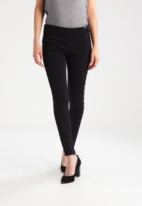 Czarne legginsy o dopasowanym kroju, z metalowymi zapięciami wzdłuż boków, wykonane z elastycznego materiału dla zapewnienia komfortu.