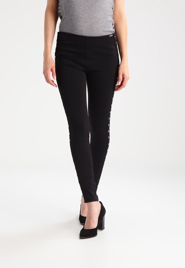 Czarne legginsy o dopasowanym kroju, z metalowymi zapięciami wzdłuż boków, wykonane z elastycznego materiału dla zapewnienia komfortu.