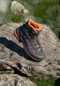 Dunkelgrauer Wanderschuh mit orangen Akzenten, gepolstertem Kragen, strukturiertem Obermaterial und kontrastierenden Schnürsenkeln. Verfügt über eine Gummisohle für bessere Traktion.