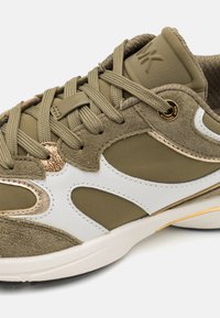 Olivengrønne sneakers lavet af ruskind og stofmaterialer, med hvide accenter, gyldent hardware og tekstureret snøredesign. Har en tykk hvid sål.
