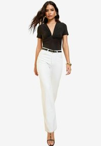 Černý bodysuit s krátkým rukávem a twist detail, doplněný bílými džíny s vysokým pasem. Outfit je doplněn černým pásem a sandály na podpatku.