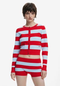 Cardigan cropped în dungi roșii și albastre deschise, cu nasturi și pantaloni scurți asortați, realizat dintr-un material tricotat cu nervuri. Include text brodat.