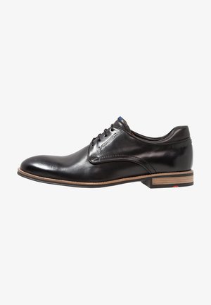Chaussure habillée pour homme en cuir noir poli avec fermeture à lacets et talon empilé en bois, vue de profil sur fond blanc.