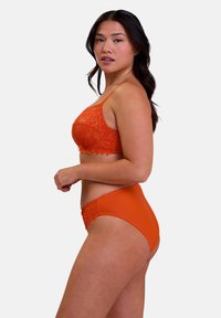 Bralette arancione in pizzo con culotte alte abbinate. Il bralette presenta dettagli in pizzo intricati con bordi ondulati e spalline sottili.