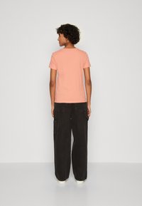 Ferskenfarvet t-shirt med korte ærmer og rund hals, parret med løsthængende sorte cargo-bukser med sidelommer og en tekstureret overflade.