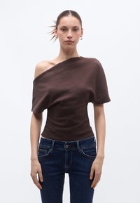 Καφέ τοπ με ανοιχτούς ώμους από μα λακό, ελαστικό ύφασμα, σε συνδυασμό με σκούρο μπλε τζιν με διακριτικές ραφές και κουμπιά μπροστά.