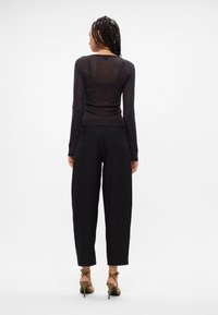 Top negro transparente de manga larga con patrón de puntos, combinado con pantalones negros holgados y sandalias de tacón bajo. Diseño minimalista con líneas limpias.