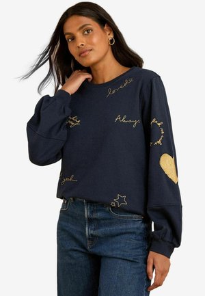 Marineblaues Sweatshirt mit goldenen gestickten Phrasen und Designs, einschließlich Herz- und Sternakzenten. Puffärmel und lockere Passform.