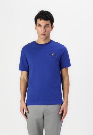 T-shirt en coton bleu avec un col rond et des manches courtes. Présente un petit logo brodé sur la poitrine gauche. Texture lisse.