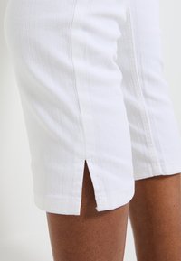 Shorts de mezclilla blanca con un ajuste ceñido, que presentan un detalle de abertura lateral en el dobladillo. La tela tiene una ligera textura y una apariencia resistente.