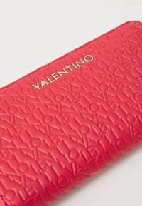 Raudonas tekstūruotas piniginė su iškilniu "Valentino" prekės ženklu ir pakartotiniais raštais. Lygus paviršius su elegantiška, stačiakampio forma.