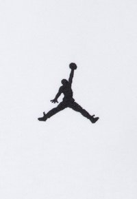 Μαύρο κεντητό λογότυπο Jumpman σε άσπρο ύφασμα. Το λογότυπο απεικονίζει μια φιγούρα στον αέρα με μια μπάλα μπάσκετ, αναδεικνύοντας τη δυναμική κίνηση.