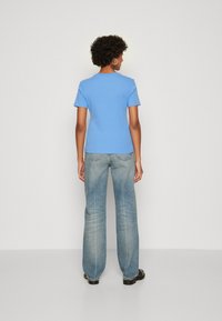 Lyseblå kortermet t-skjorte kombinert med lyse moderne vid jeans. T-skjorten har rund hals; jeansene har baklommer og en avslappet passform.