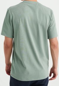 T-shirt vert clair à manches courtes, en coton doux, avec un col rond et une coupe décontractée, présentant une texture lisse et uniforme.