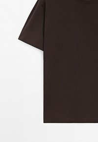 T-shirt en coton marron foncé à manches courtes avec col rond présenté sur fond blanc, montrant le côté gauche et la manche.