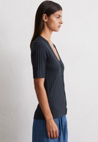 Granatowa bluzka z krótkim rękawem i głębokim dekoltem w serek, z guzikami z przodu. Materiał jest gładki z fakturowanym wzorem.