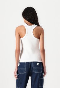 Balti raštuota tank top su lenktu nugaros dizainu. Audinys yra lygus ir prigludęs, pabrėžiantis paprastą ir švarią siluetą.
