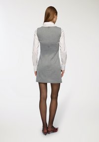 Vestito grigio aderente con colletto e zip sul retro, abbinato a una camicia bianca a maniche lunghe, collant neri e scarpe con tacco rosse.