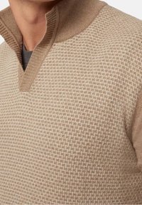 Béžový pletený pulovr se strukturovaným vzorem, s límcem na poloviční zip a žebrovanými manžetami, vyrobený z měkké látky.