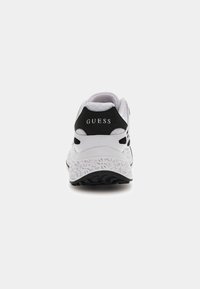 Vista posteriore di una sneaker Guess bianca e nera con suola decorata e nome del marchio sul tallone, su sfondo neutro.