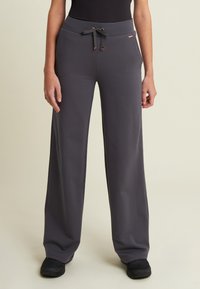 Pantalones de pierna ancha grises, confeccionados en tejido suave, con cintura elástica, cordón de ajuste con herrajes metálicos y bolsillos laterales.