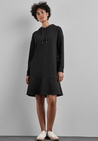 Robe à capuche noire avec des manches longues et un ourlet évasé. Fabriquée en tissu doux, elle possède une capuche avec cordon de serrage et des poignets simples.