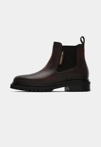 Bota Chelsea em pele castanha escura com painel lateral elástico preto, aba de puxar, sola robusta e etiqueta com o logótipo de Karl Lagerfeld na lateral.