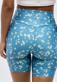 Κοντινό ενός ατόμου που φοράει μπλε ποδηλατικά σορτς με ψηλή μέση, με ανοιχτές αφηρημένες κηλίδες και το λογότυπο "ONLY PLAY" στη ζώνη μέσης.