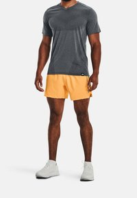 Camiseta atlética de manga corta gris con rayas texturizadas y cuello en V, combinada con pantalones cortos naranja brillante. Zapatillas deportivas blancas completan el conjunto.